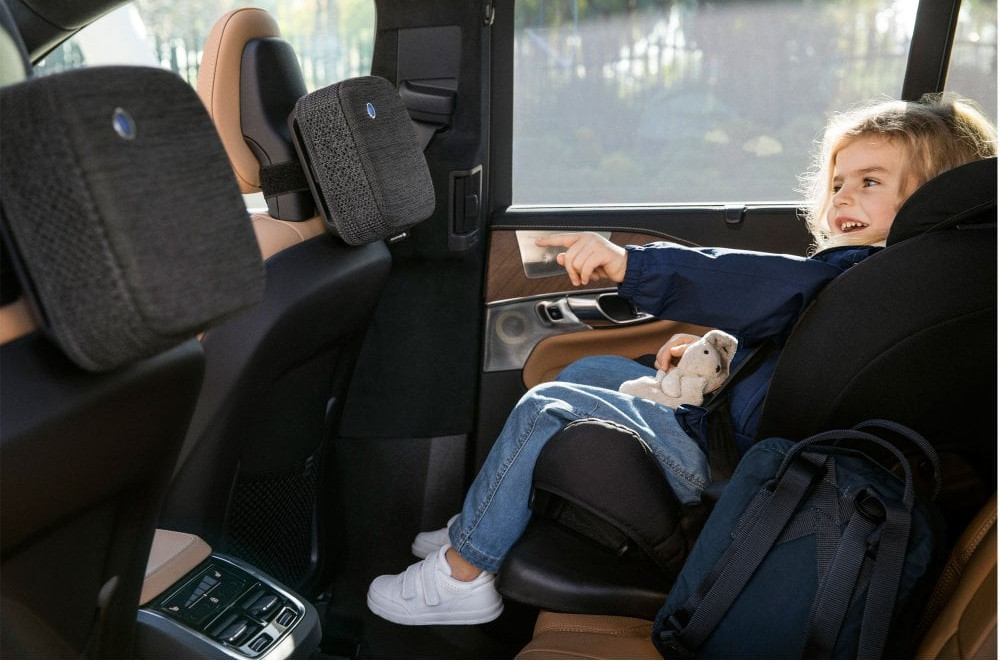 A child in a car seat points, with a backpack and headrest visible.