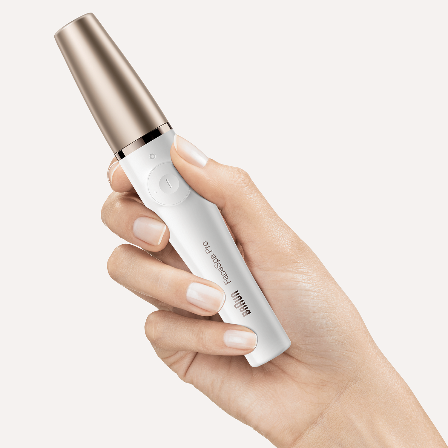 Een hand die een witte en roségouden Braun FaceSpa Pro vasthoudt, het apparaat staat aan.