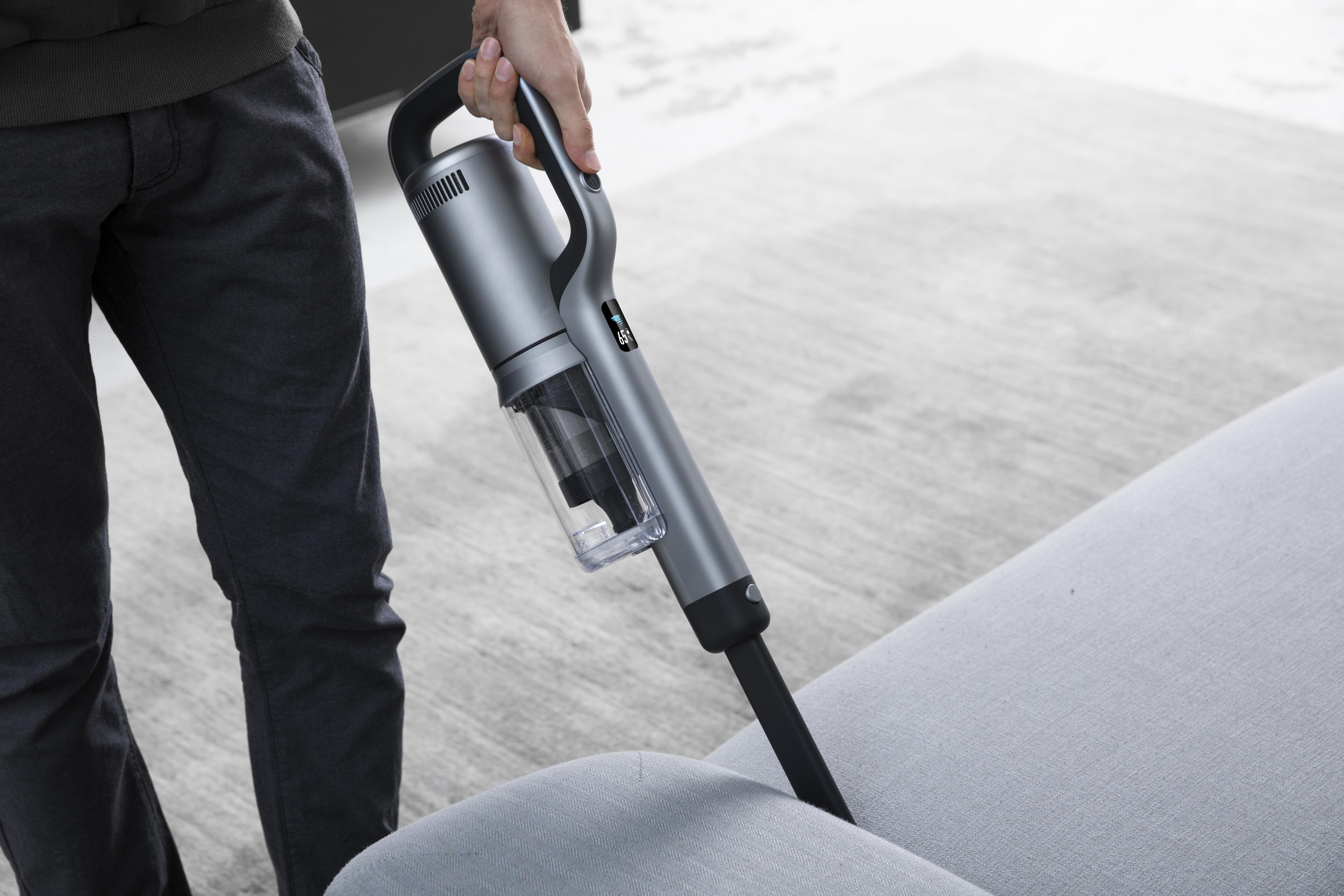 Eine Person, die ein graues Sofa mit einem kabellosen Handstaubsauger reinigt.