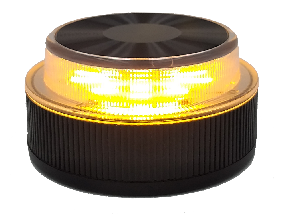 Una luz de advertencia ámbar, base negra, borde plateado. La luz está encendida, amarillo brillante.