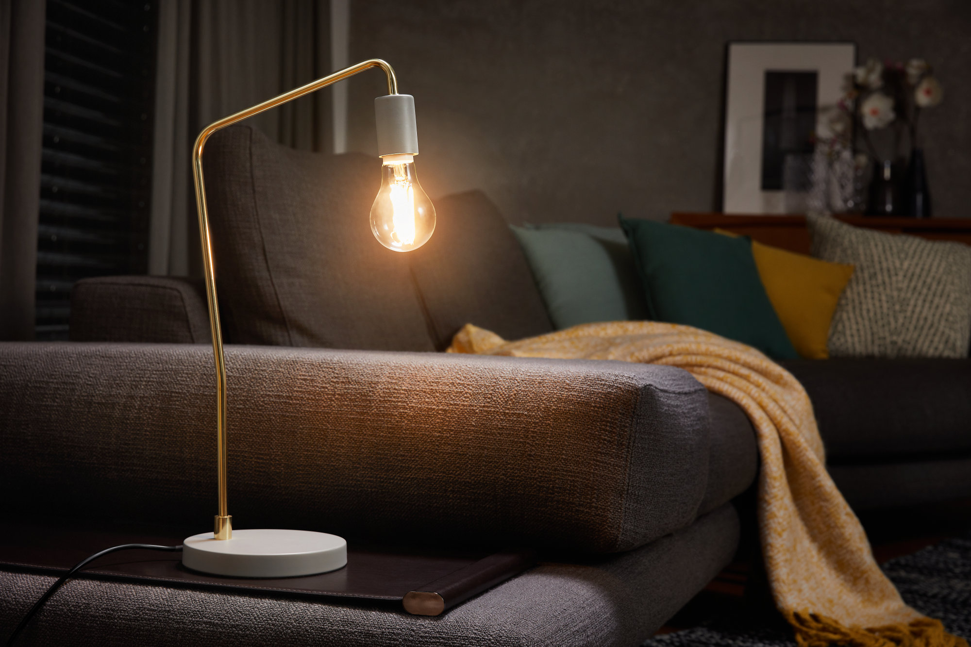 Tischlampe mit goldenem Rahmen, weißem Sockel und sichtbarer Glühbirne.