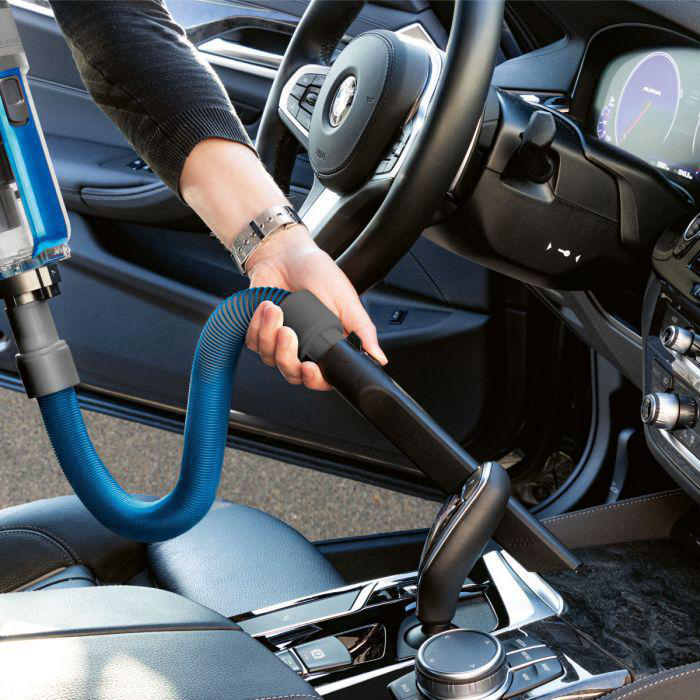 Eine Person reinigt mit einem blauen Staubsaugerschlauch das Innere eines Autos.