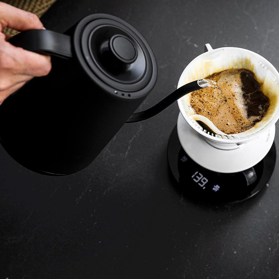 Ein schwarzer Wasserkocher gießt Wasser in einen weißen Pour-Over-Kaffeebereiter.