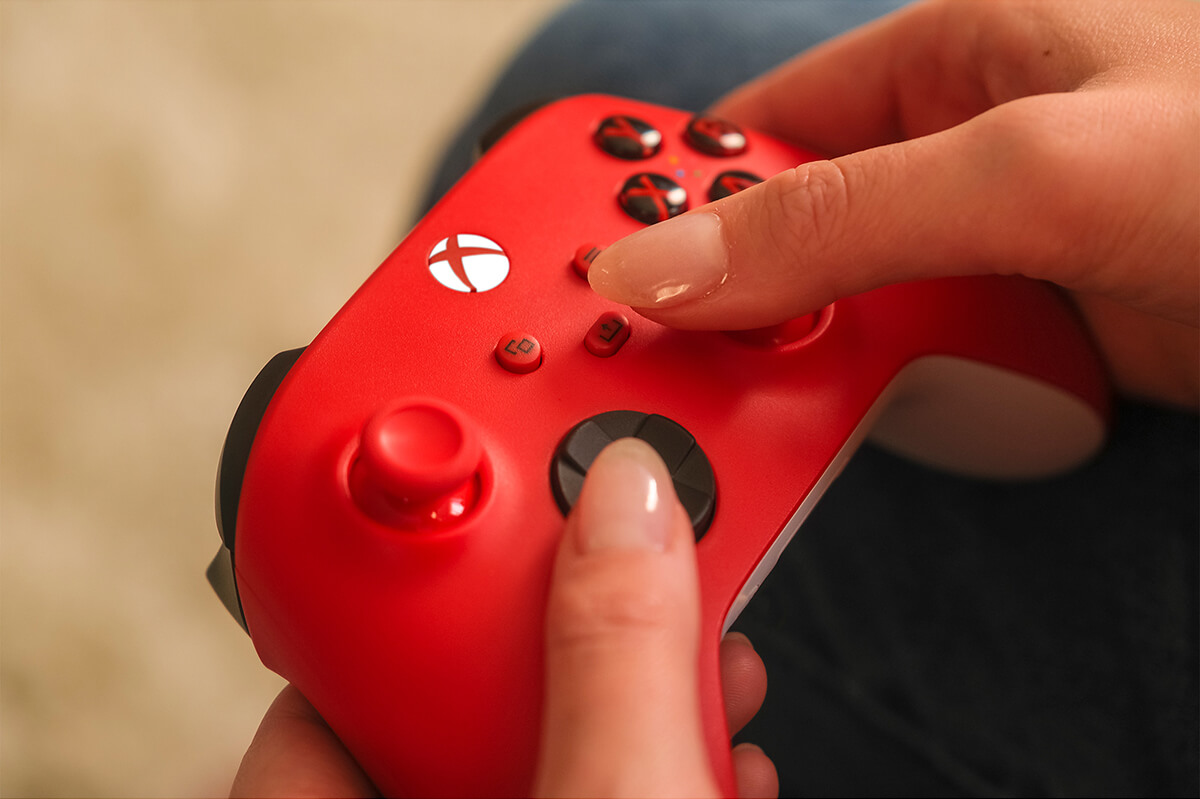 A person holding a red Xbox controller. The person is about to press a button.