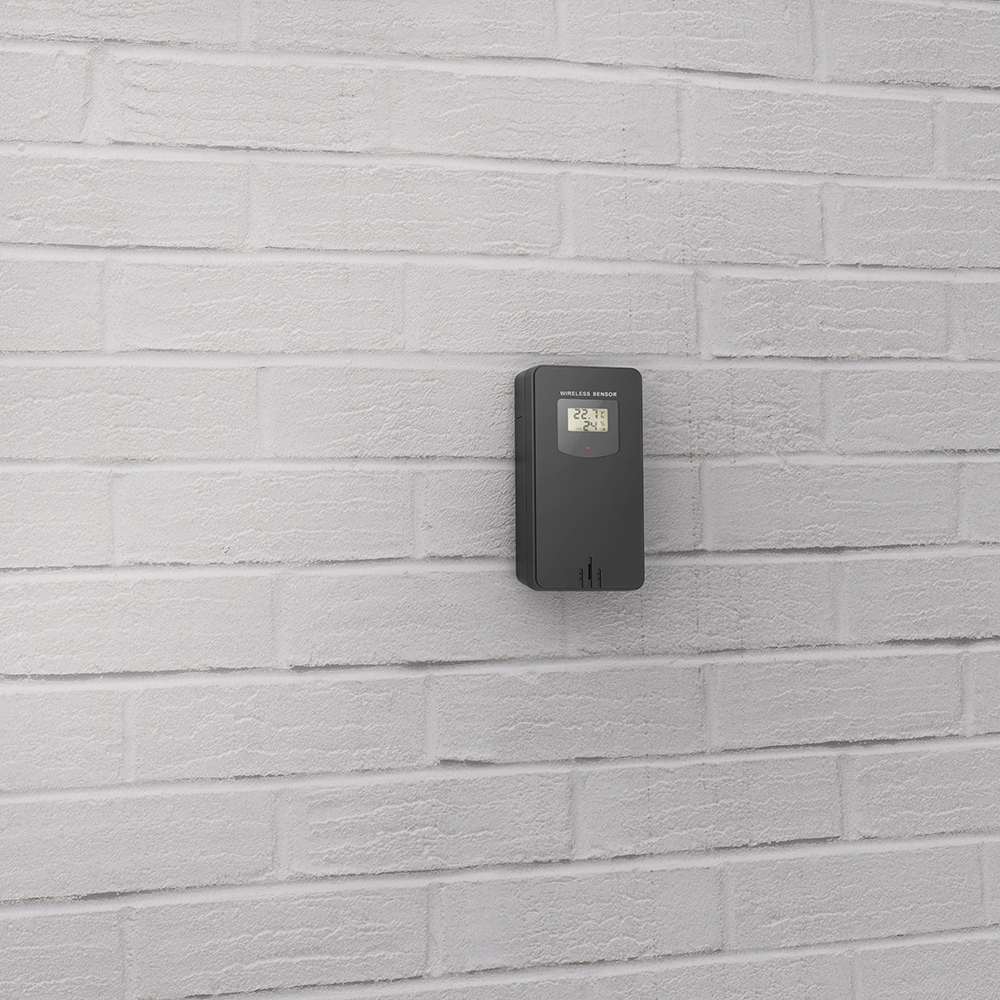 Outdoor temperature sensor mounted on a white brick wall, displaying 22.1 and 24.