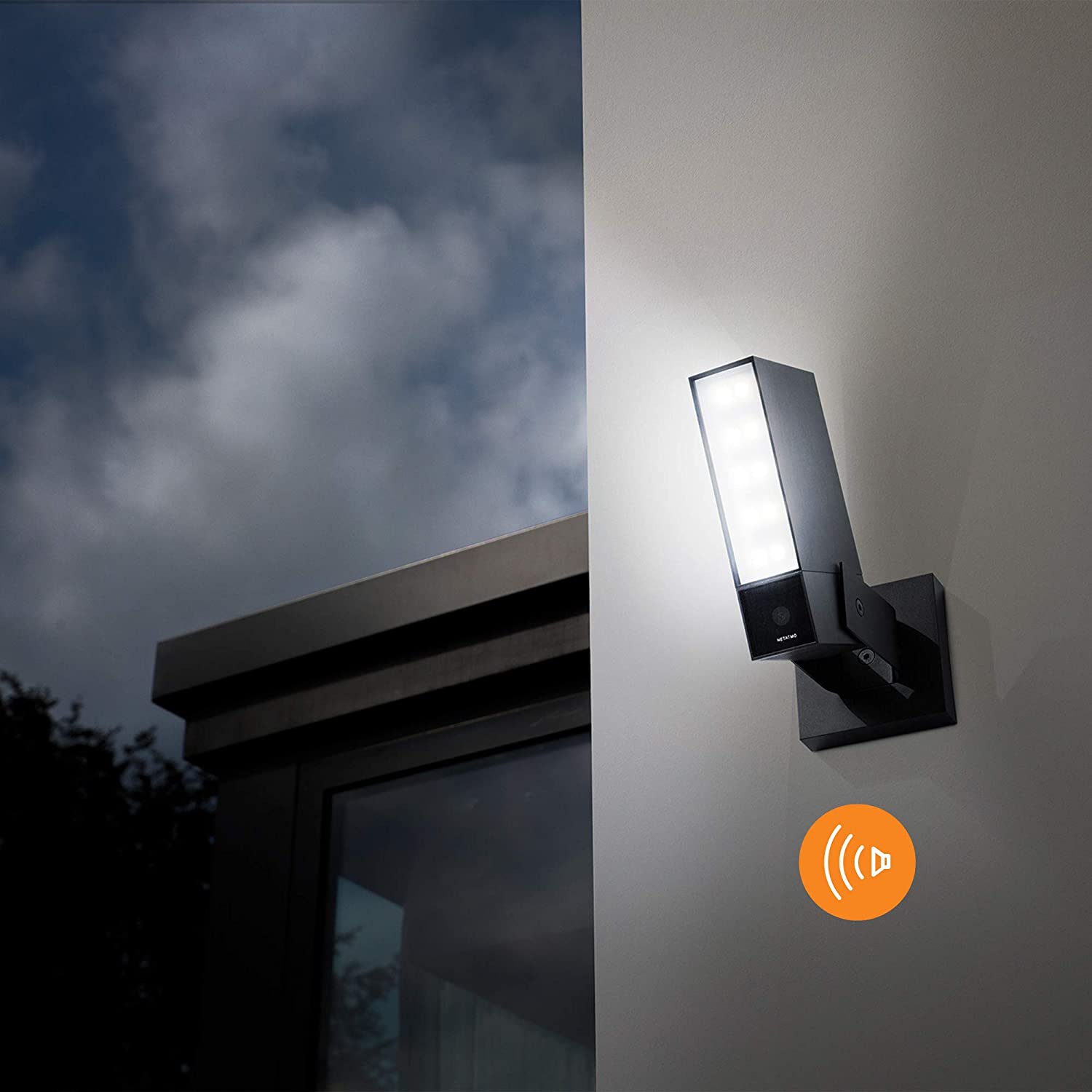 Une lumière de sécurité fixée à un mur, avec un ciel nuageux en arrière-plan. Un symbole d'onde sonore est présent.
