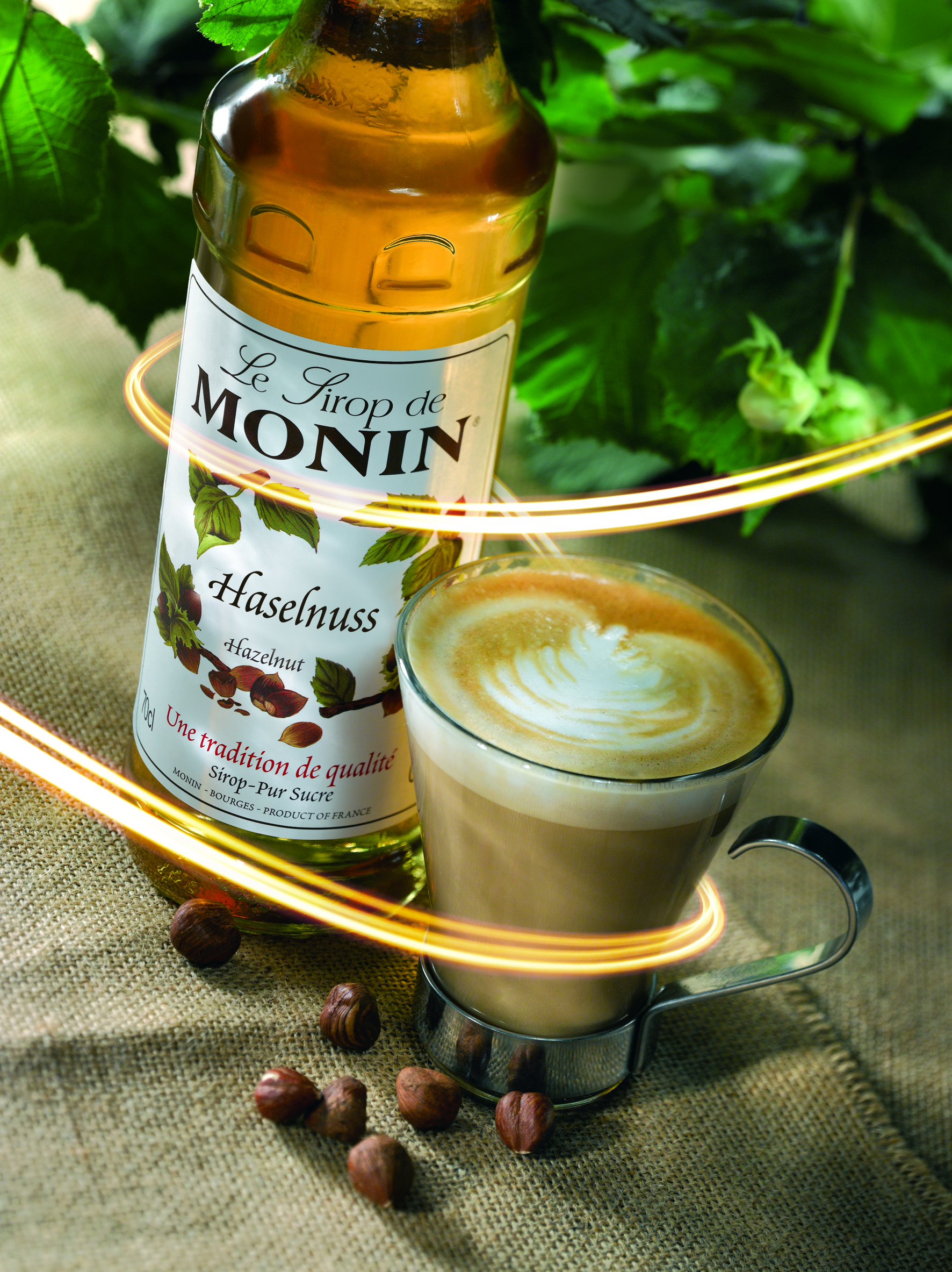 Eine Flasche Monin Haselnusssirup neben einem Latte. Brauner Hintergrund.