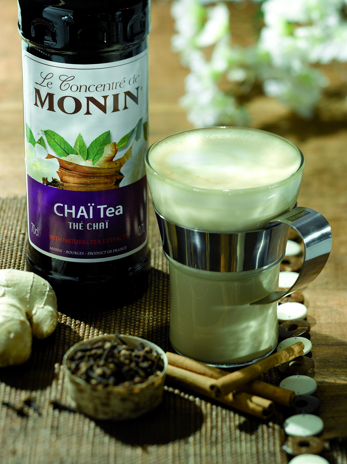 Chai-Tee mit Zutaten: Monin-Sirup, Tee, Ingwer und Zimtstangen. Ein Glas mit Schaum.