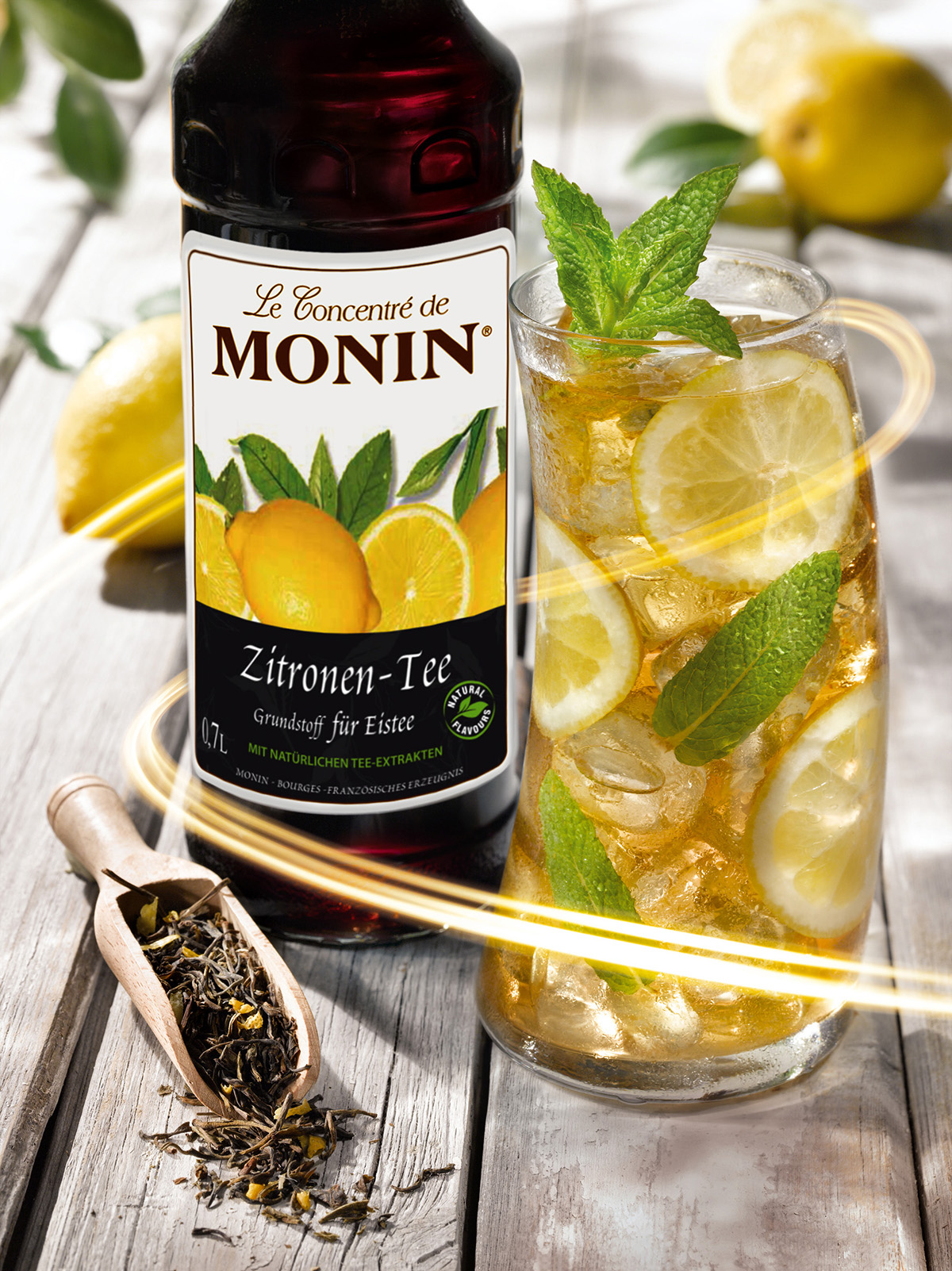 Monin-Flasche, Zitronenscheiben und Eistee. Minzblätter und ein Holzlöffel mit Teeblättern.