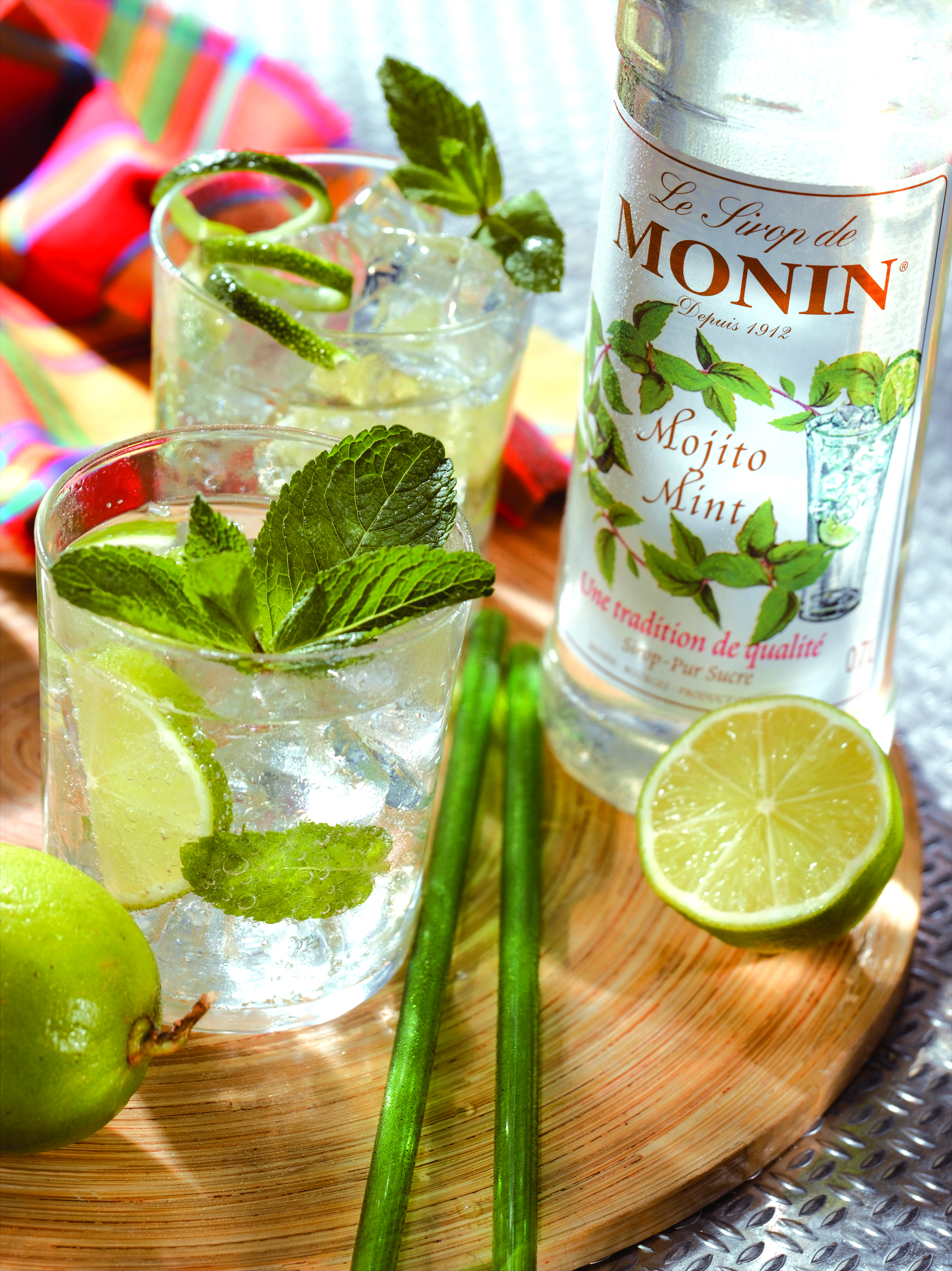 Zwei Gläser mit Mojito-Cocktails, Limette, Minze und eine Flasche Monin Mojito Mint.