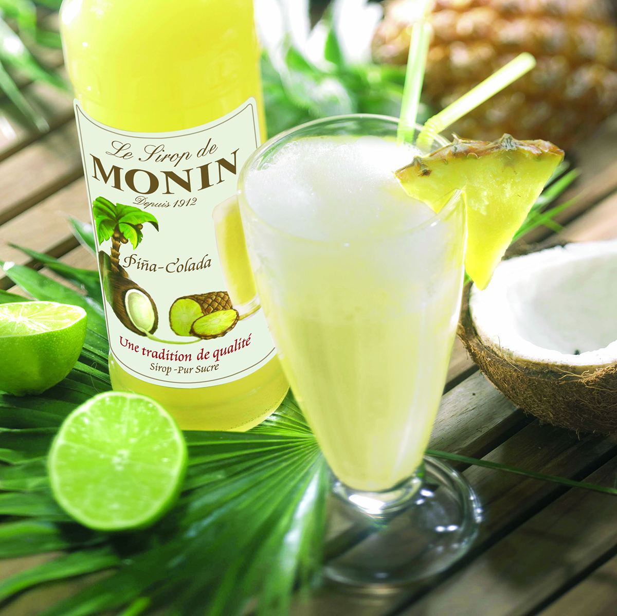 Eine Monin-Flasche, ein Piña Colada-Getränk, Kokosnuss, Limette und Ananasscheibe.