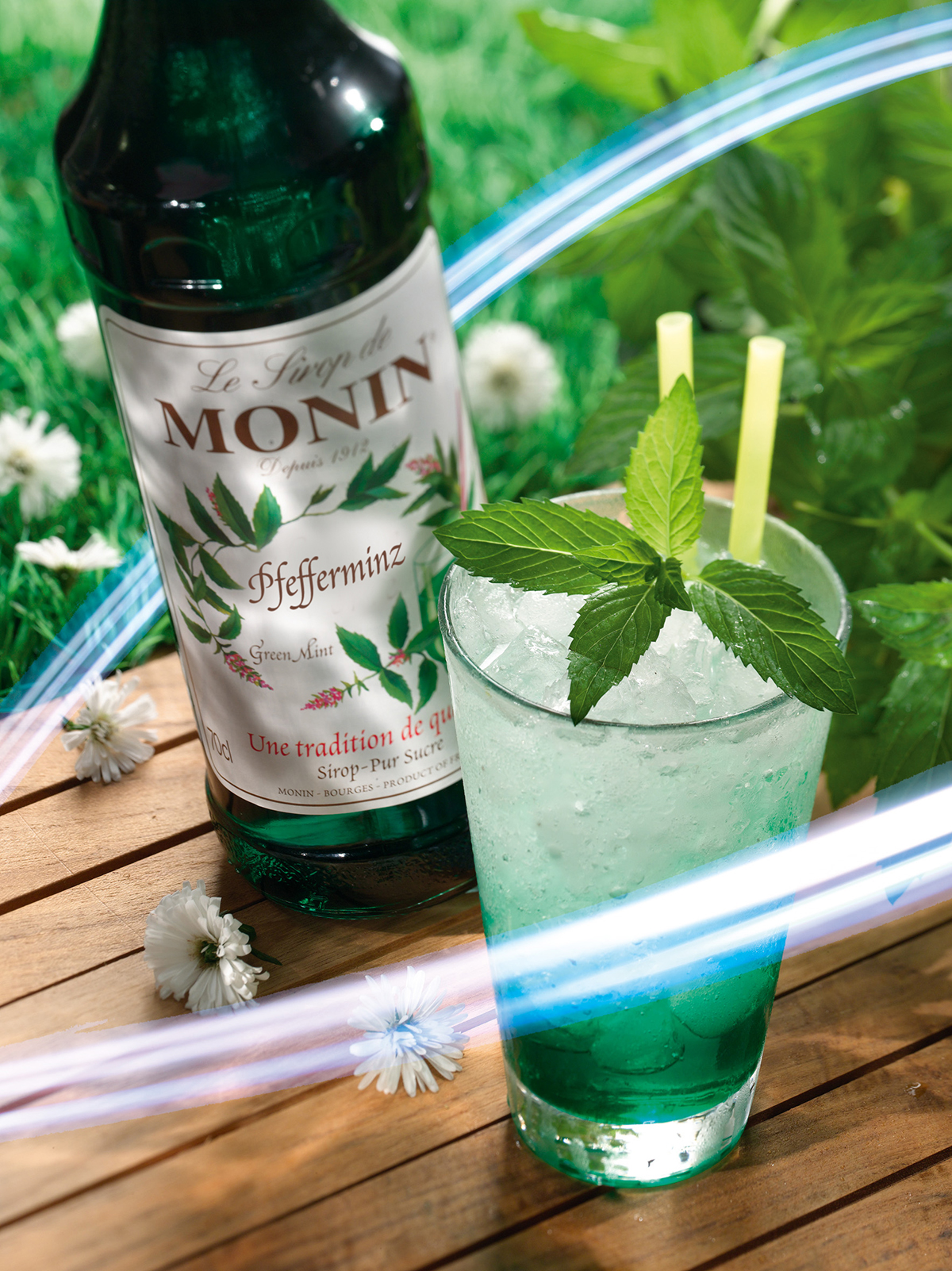 Ein Minzcocktail mit Minze, Eis und Strohhalmen. Eine Flasche Monin-Sirup daneben.