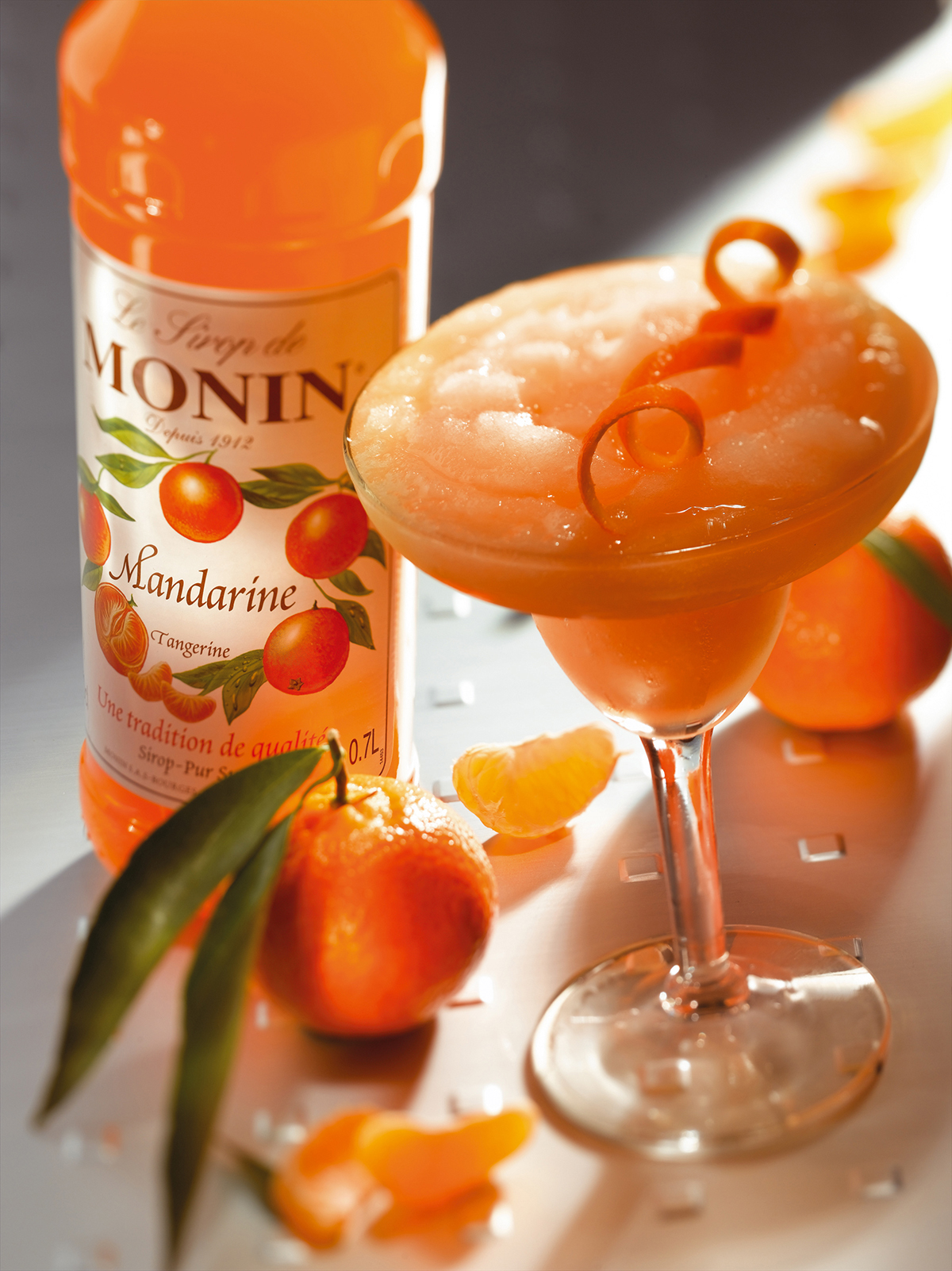 Eine Monin Mandarinen-Sirupflasche und ein Cocktail in einem Glas.