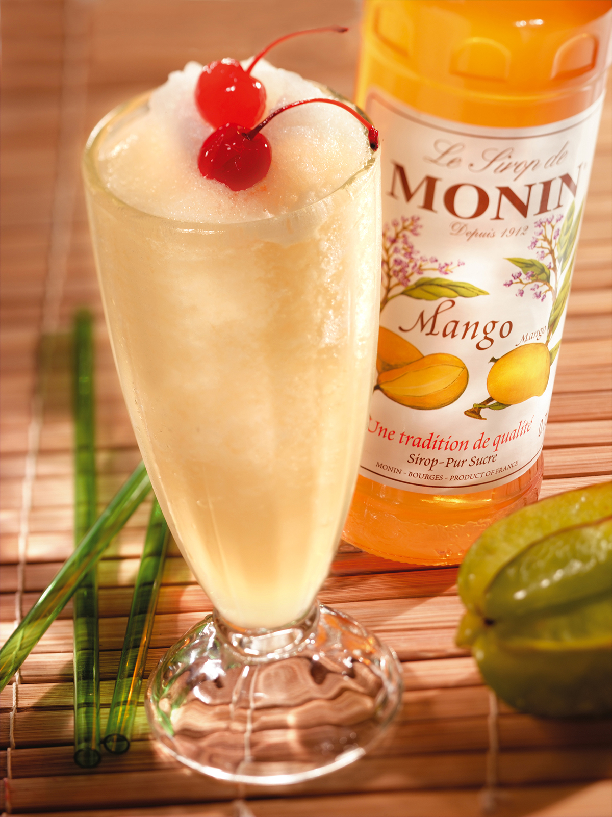 Mango-Smoothie im Glas mit Kirschen und einer Monin-Flasche.
