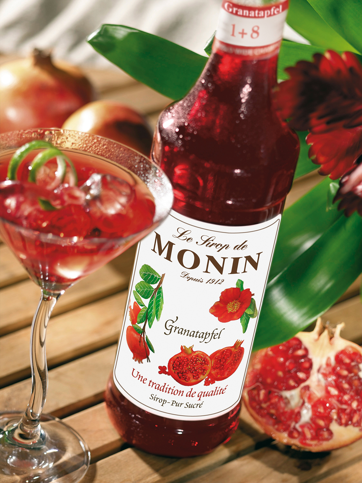 Granatapfel-Cocktail mit Monin-Sirup, Granatapfel und Blumen auf Holzoberfläche.