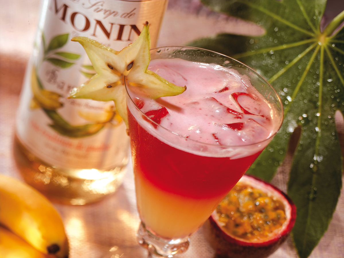 Tropischer Cocktail mit Monin-Sirup, Sternfrucht, Passionsfrucht und Banane auf einem Blatt.