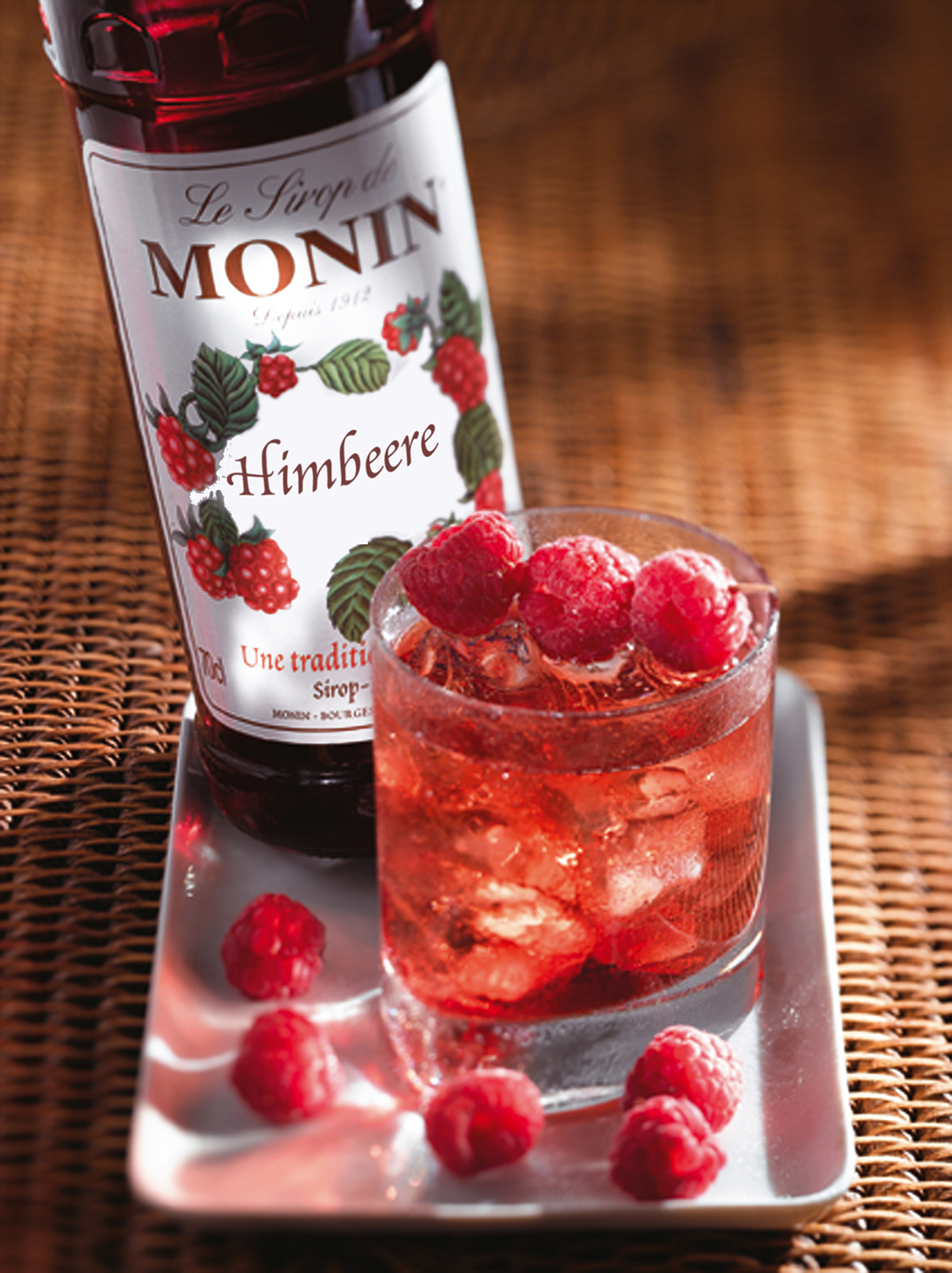 Ein Glas Himbeergetränk mit Himbeeren und eine Flasche Monin-Sirup.