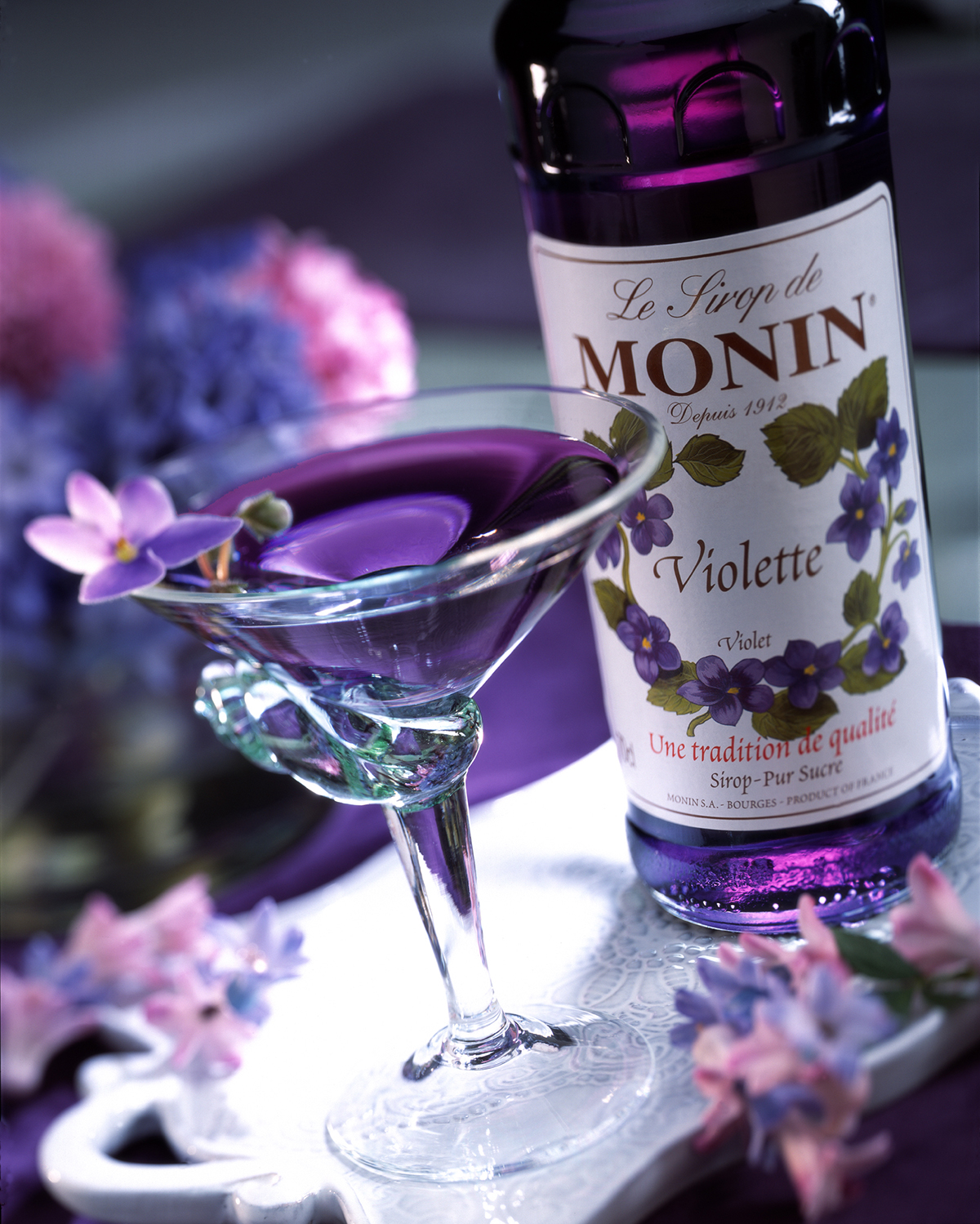 Ein lila Cocktail mit einer Blume und einer Flasche daneben.