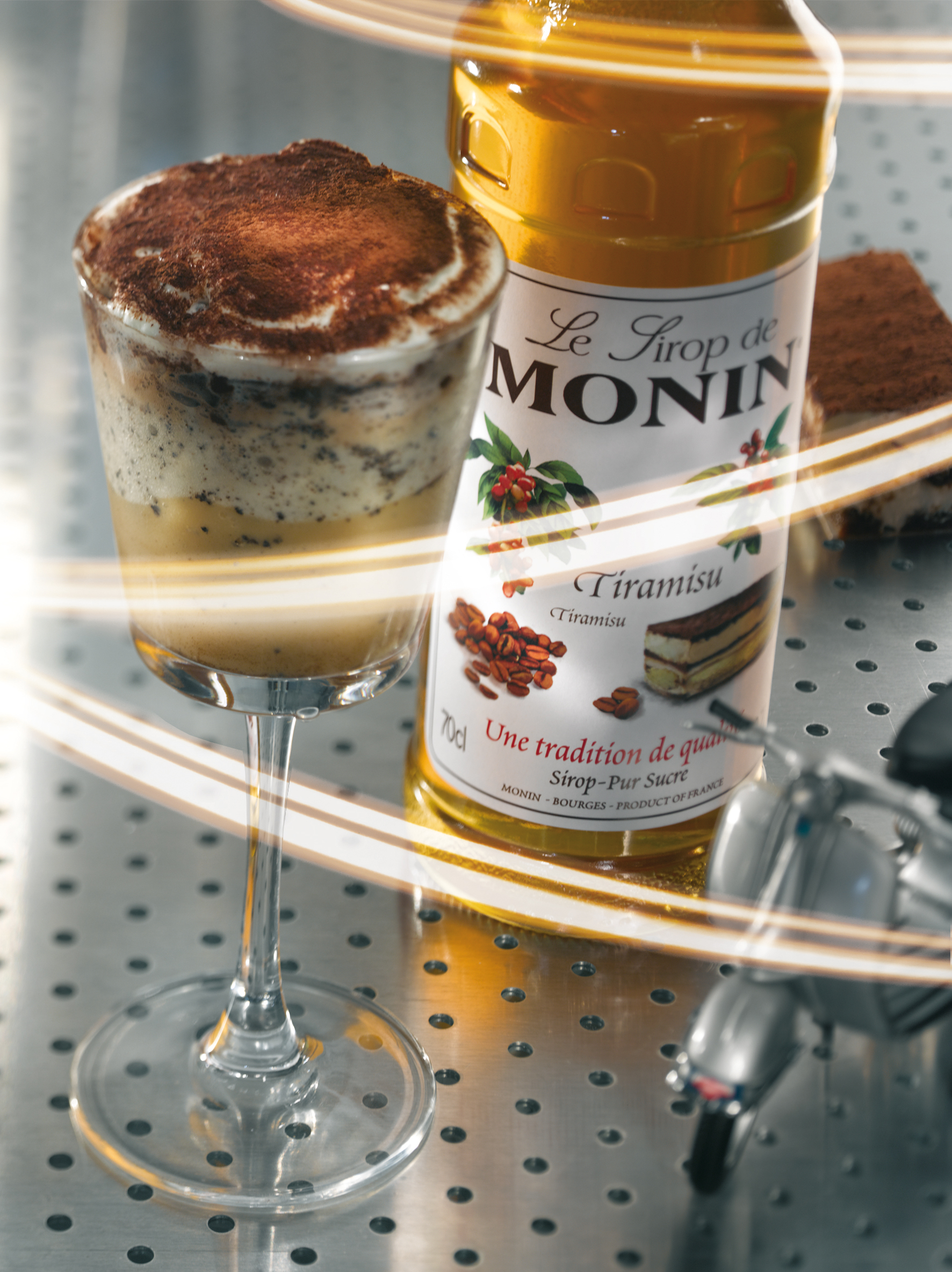 Tiramisu-Getränk im Glas, eine Sirupflasche und ein Tiramisu-Kuchen auf einer Oberfläche.