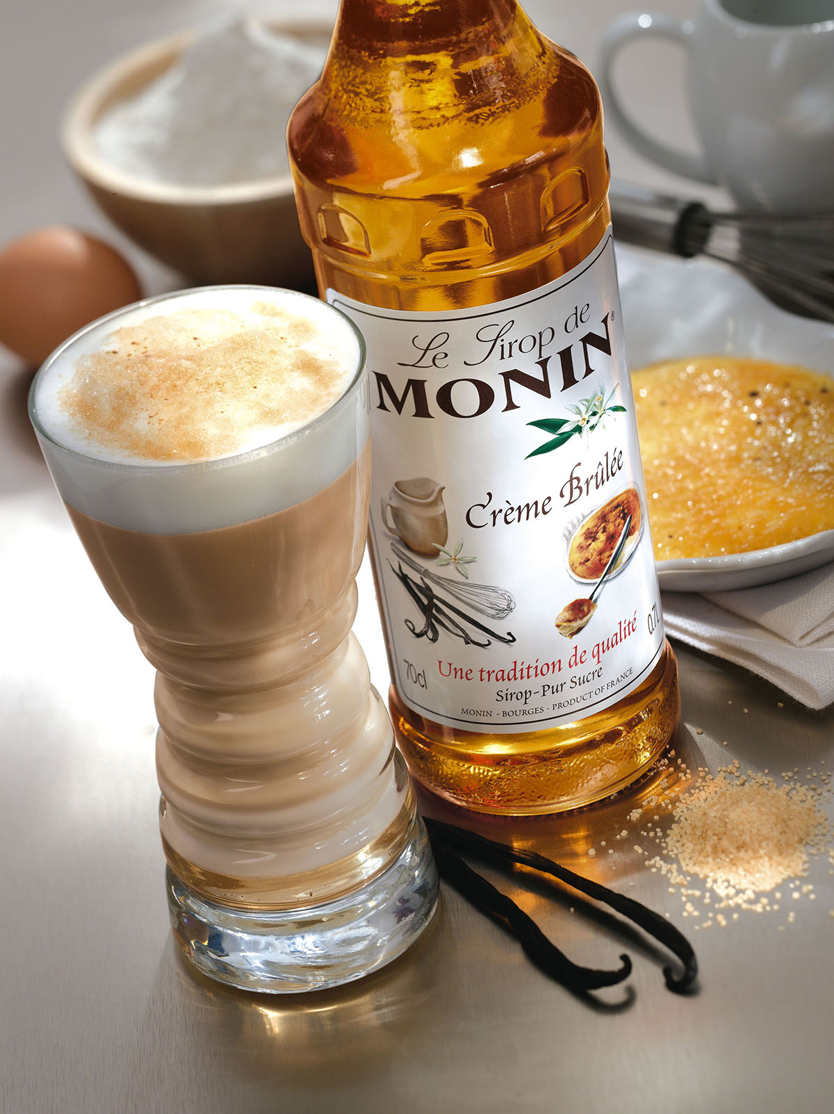 Latte Macchiato und Monin Creme Brulee Sirupflasche mit Vanilleschoten und Zucker auf der Theke.
