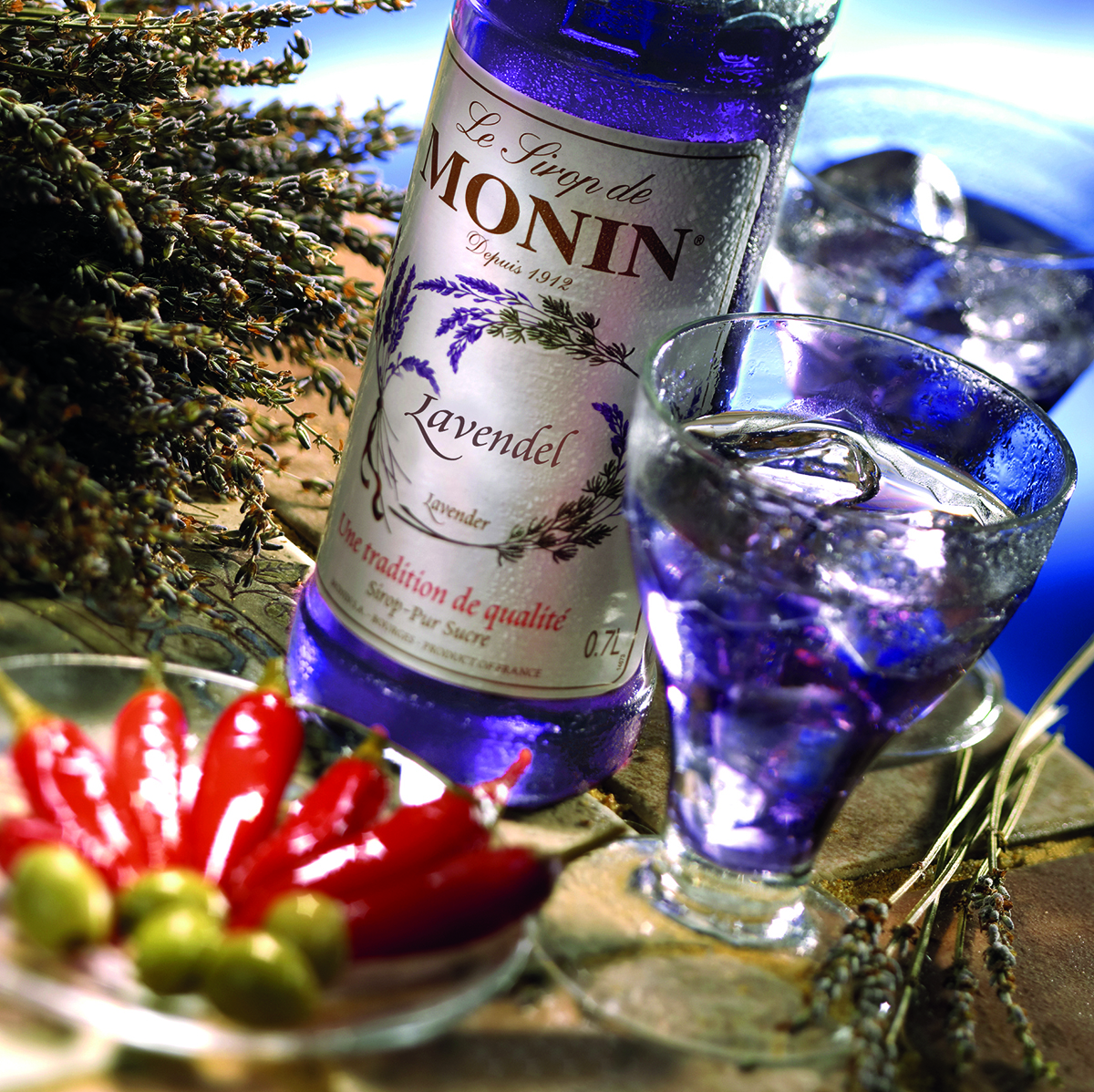 Eine Flasche Lavendelsirup, ein Glas Lavendelgetränk und rote Paprika.