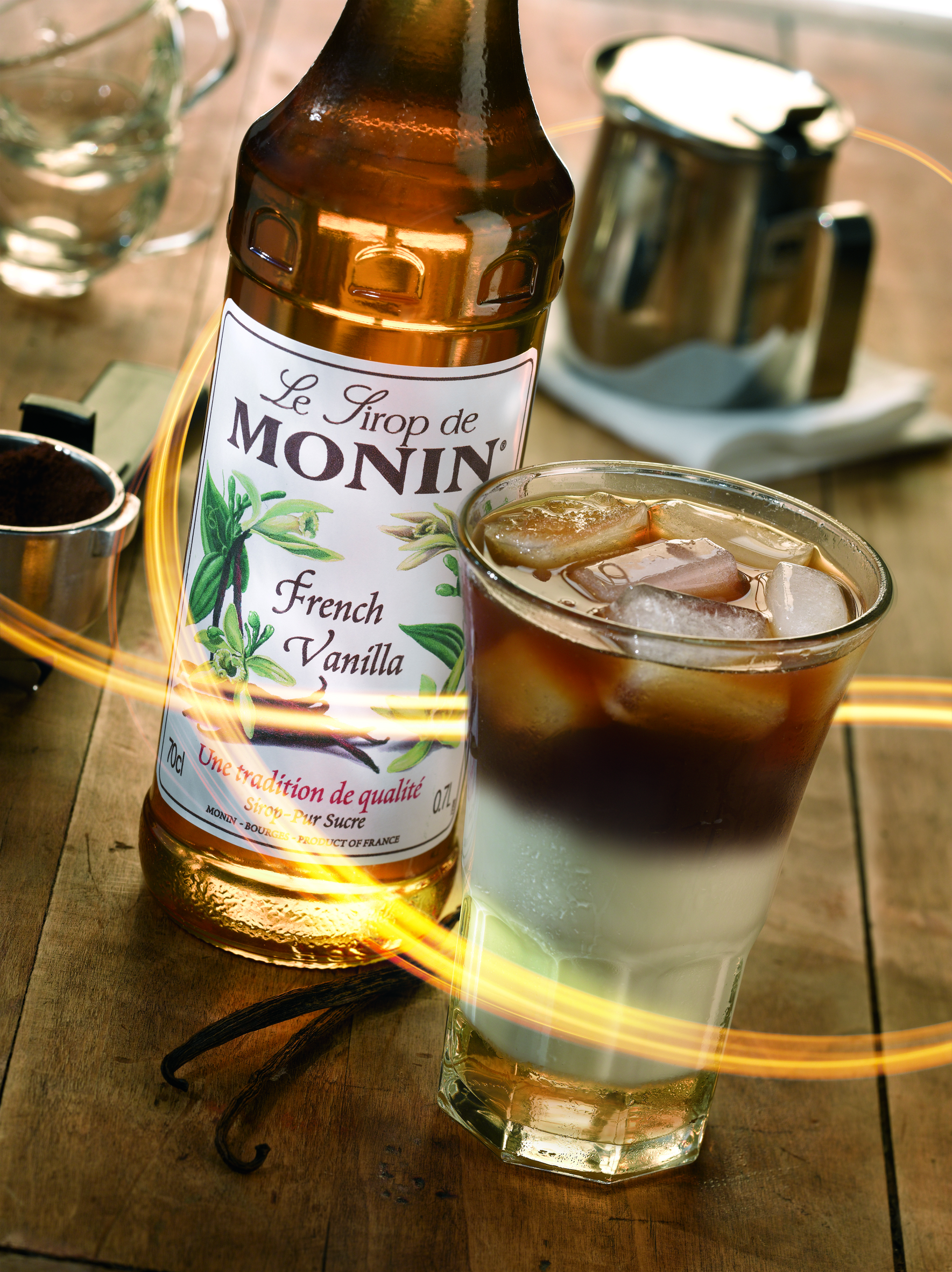 Ein Glas Eiskaffee mit Monin French Vanilla Sirup Flasche auf Holzoberfläche.