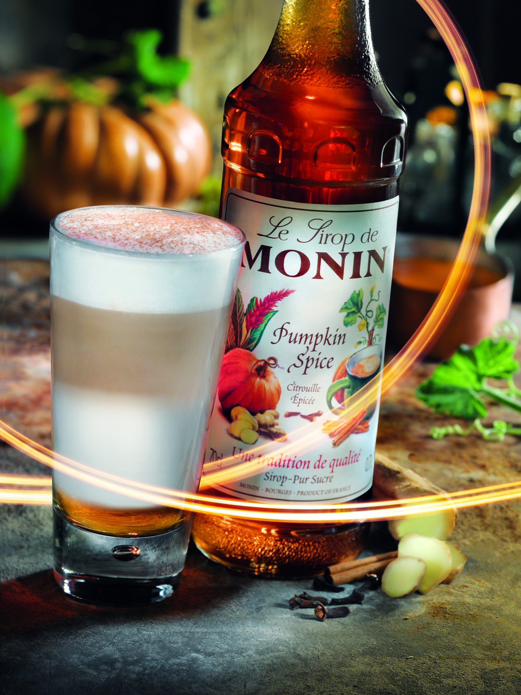 Ein Latte und eine Flasche Monin Kürbis-Gewürz-Sirup auf Holz.