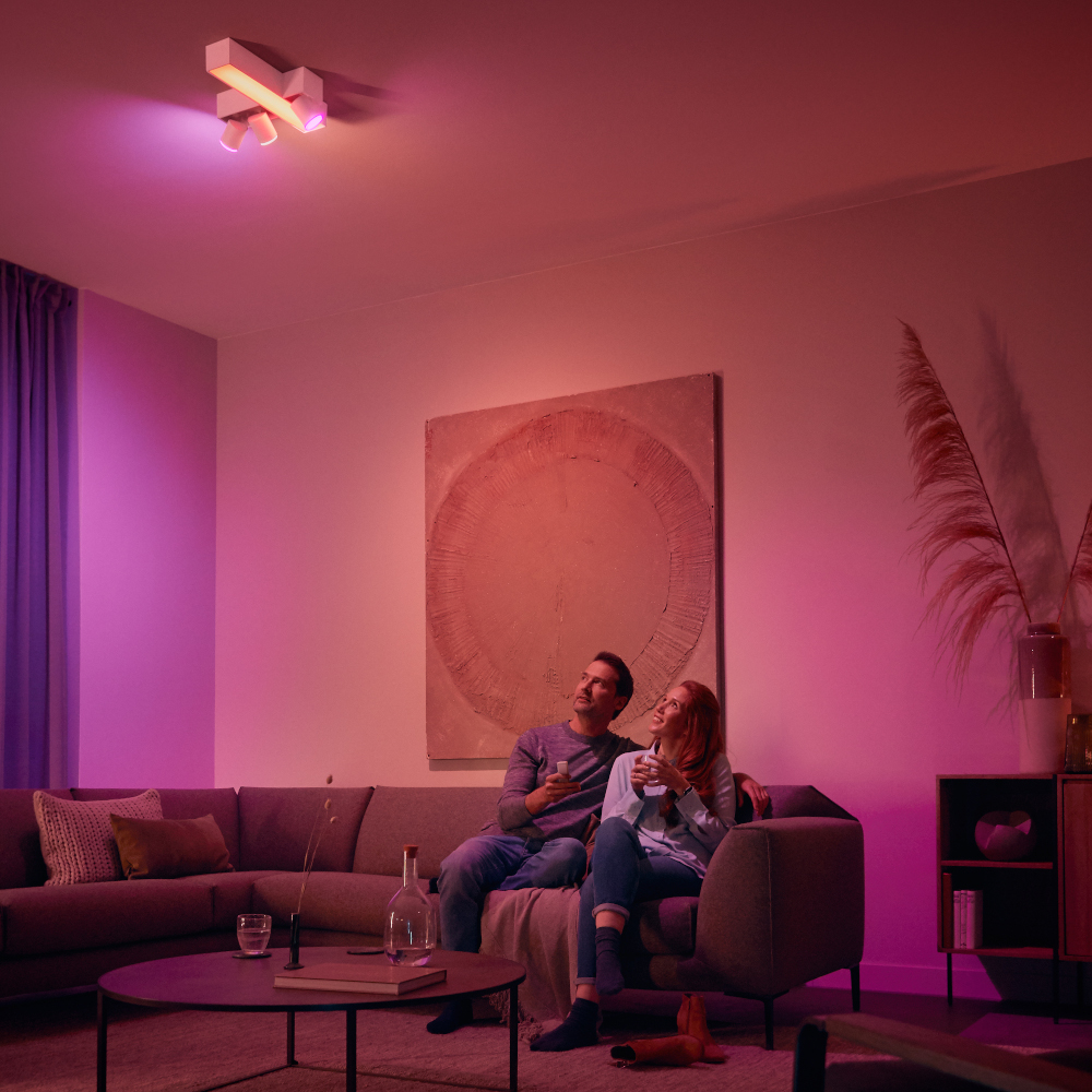 Un couple assis sur un canapé, regardant vers le haut une lumière de plafond aux teintes roses.
