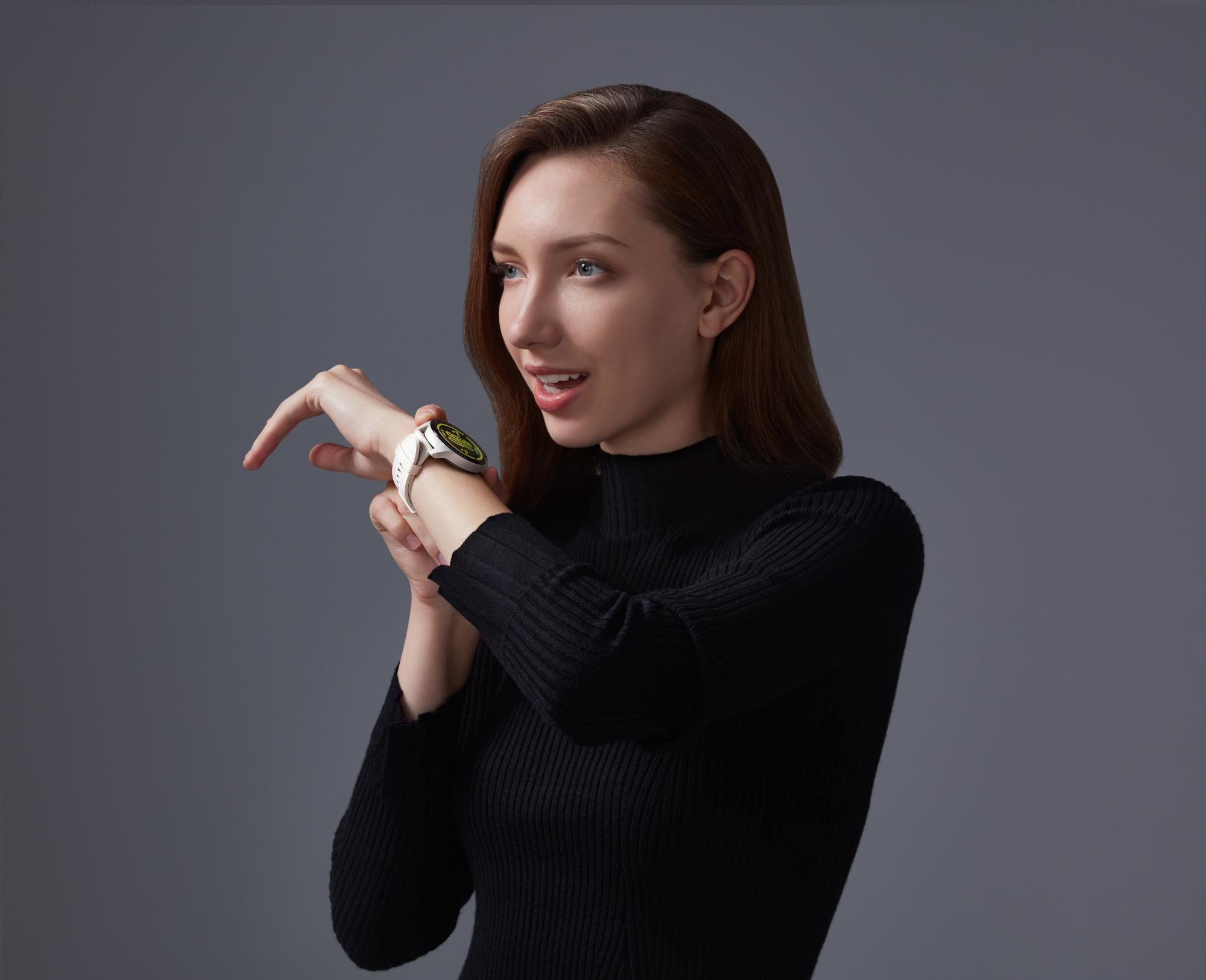 Frau, die ein schwarzes Oberteil und eine weiße Smartwatch trägt, blickt weg und lächelt.