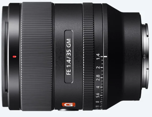 Schwarzes Kameraobjektiv. FE 1.4/35 GM an der Seite. Verschiedene Ringe mit Zahlen. Silberne und orangefarbene Akzente.