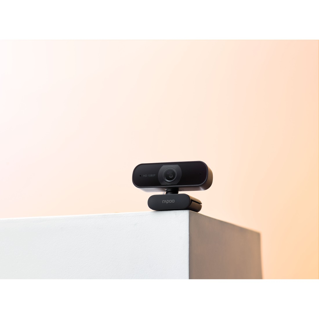 Schwarze Webcam auf weißer Oberfläche. Der Hintergrund ist ein heller Orange-Weiß-Verlauf.