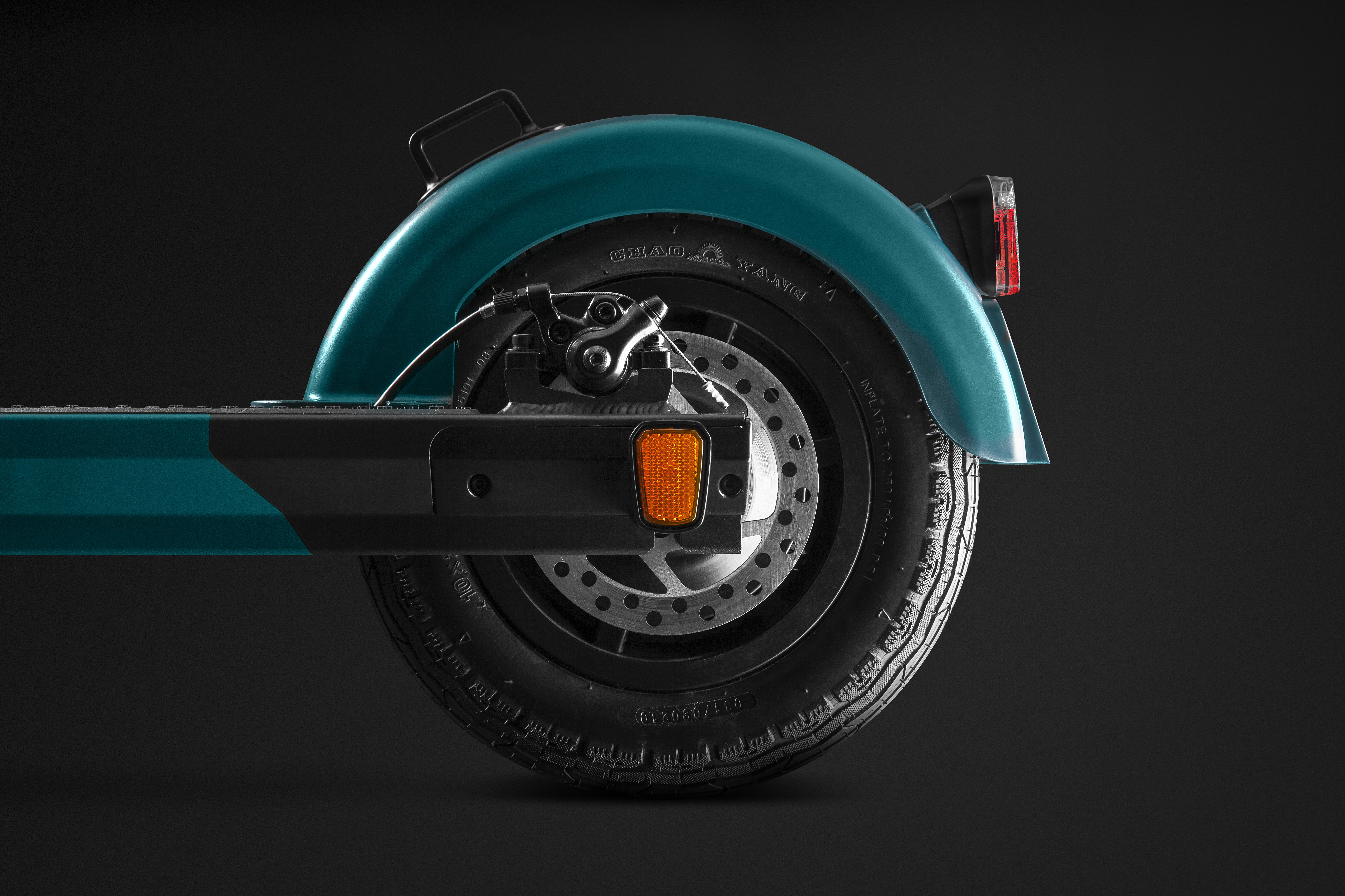 Das Hinterrad eines teal-farbenen Elektrorollers. Das Rad ist schwarz.