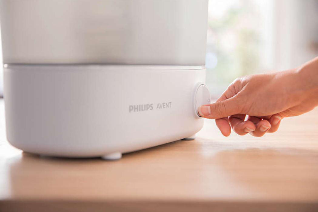 Hand drückt Knopf auf weißem Philips Avent Babyflaschensterilisator.