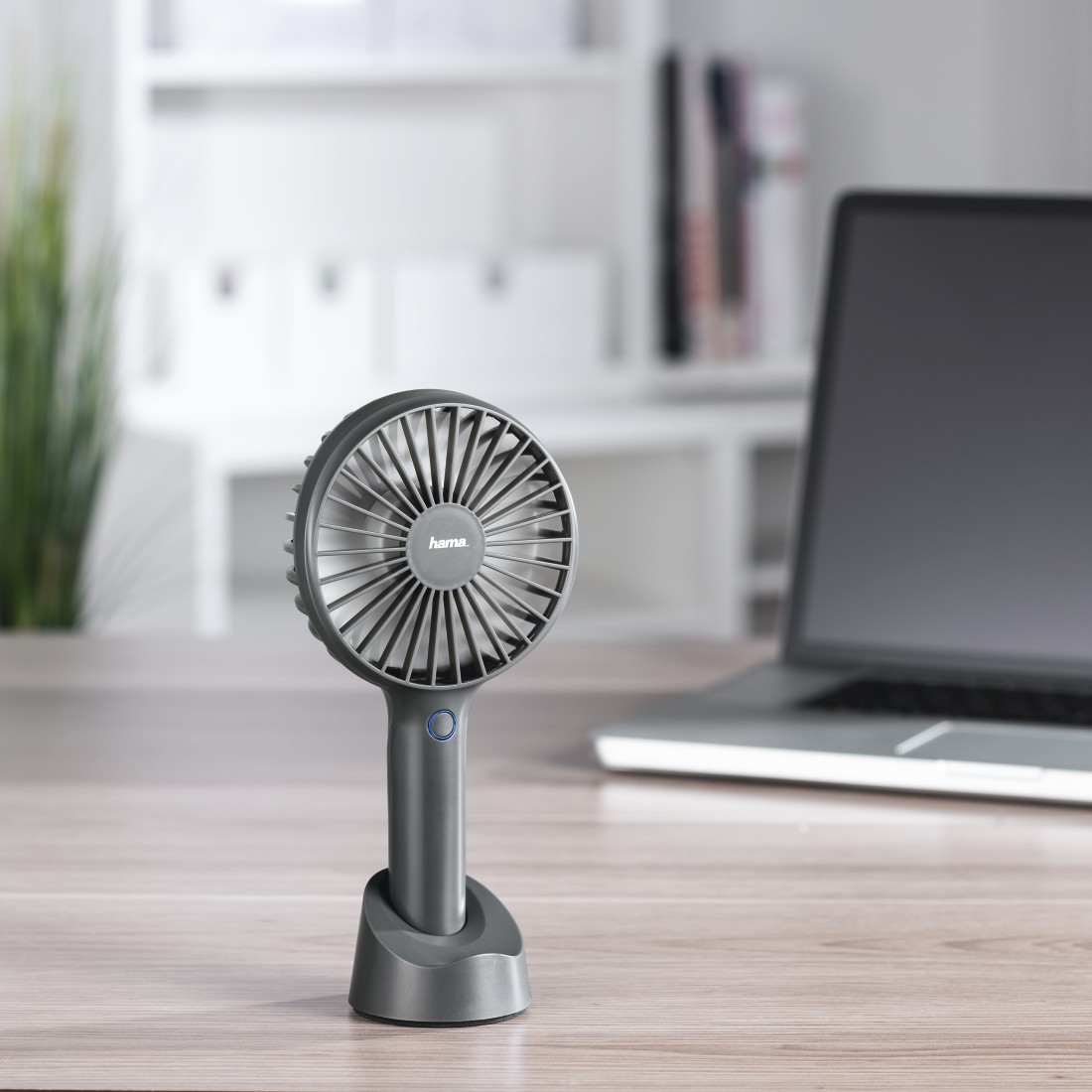 Ein kleiner grauer Ventilator auf einem grauen Ständer, auf einem Holzschreibtisch.