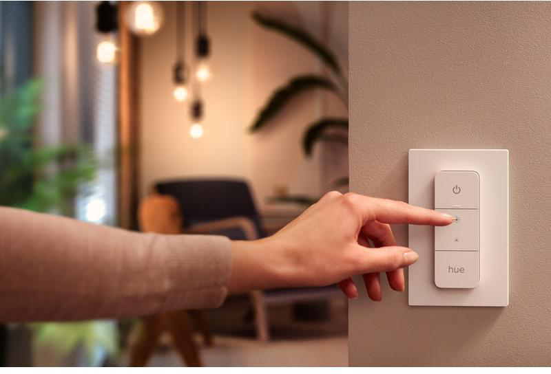 Die Hand einer Person berührt einen intelligenten Lichtschalter, im Hintergrund Deckenleuchten.