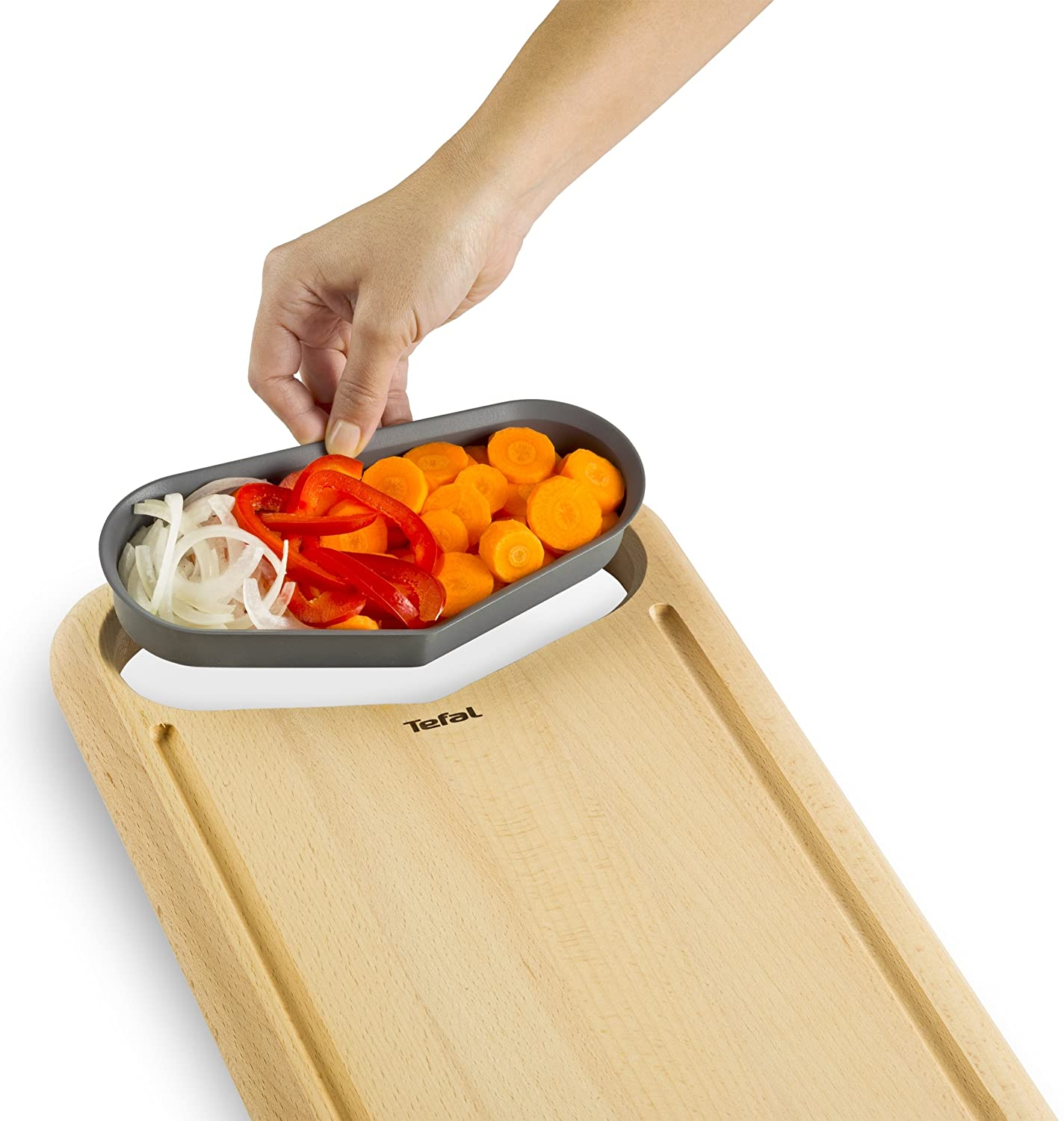 Egy kéz, amely aprított zöldségekkel teli tálcát helyez egy fadarabolódeszkára, Tefal logóval.