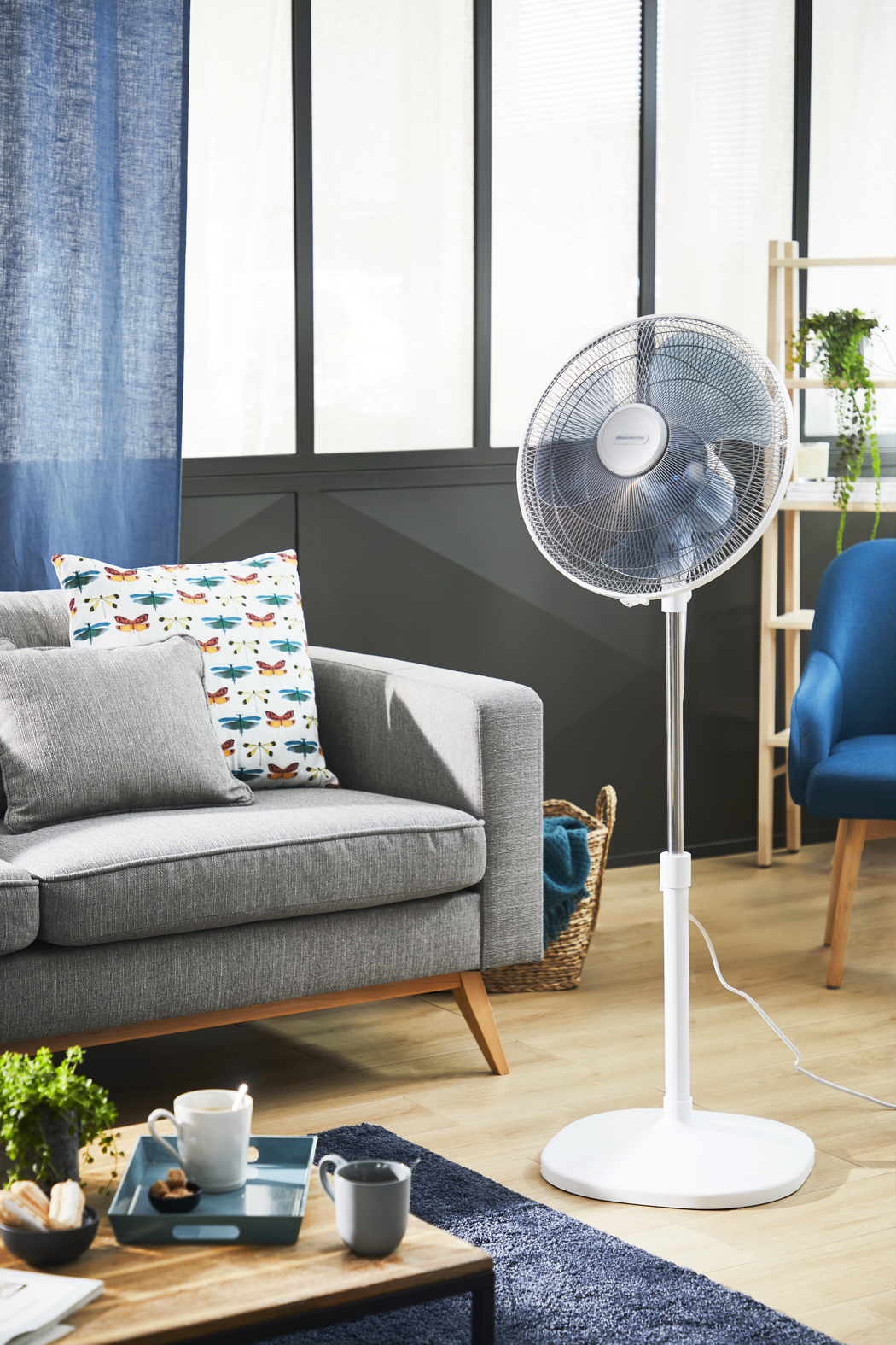Living room scene with a fan, sofa, pillows, a rug, and a blue chair.