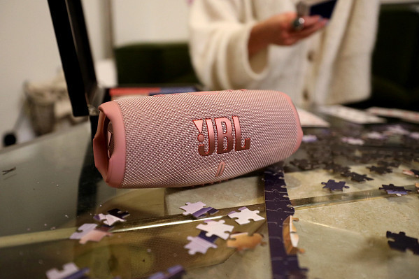 Een roze JBL-luidspreker op een tafel met puzzelstukjes en een persoon op de achtergrond.