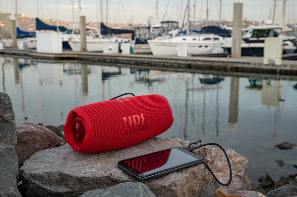 A red JBL speaker and a black smartphone with a charging cable, on a stone surface.