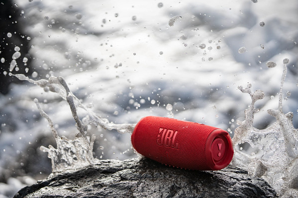 Red JBL speaker on a rock, water splashing around. Ocean background.