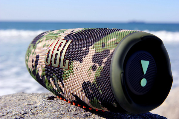 JBL-luidspreker op een rots bij de oceaan. De luidspreker is camouflage, met logo en knoppen zichtbaar.