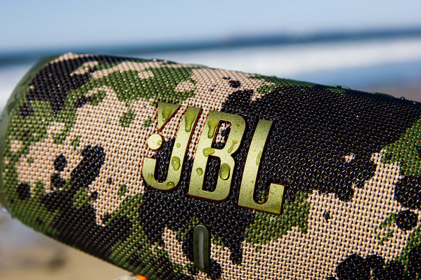 Close-up van een JBL-luidspreker met een camouflagepatroon en het JBL-logo. Waterdruppels zichtbaar.