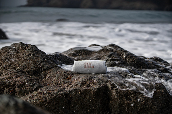 Une enceinte JBL blanche et grise sur un rocher près de l'océan.