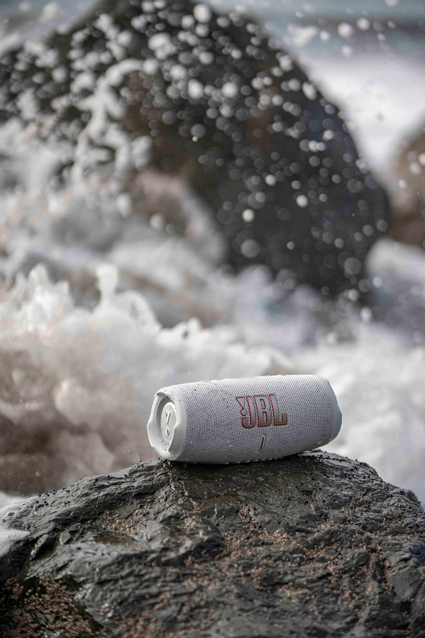 Un haut-parleur JBL blanc sur un rocher avec des vagues en arrière-plan.