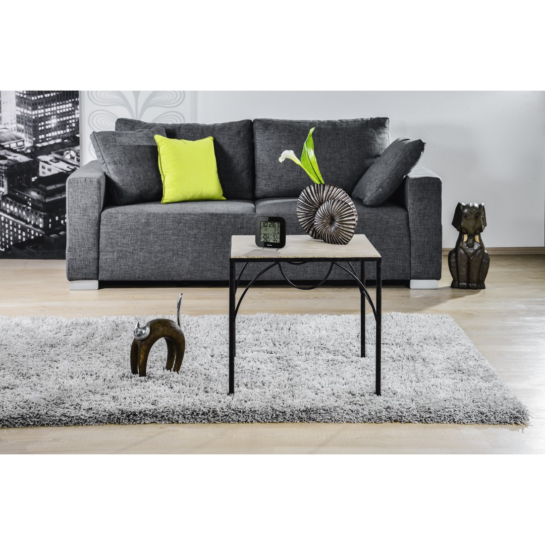 A gray sofa, a small table with a clock, a rug, and some decorative items in a living room.