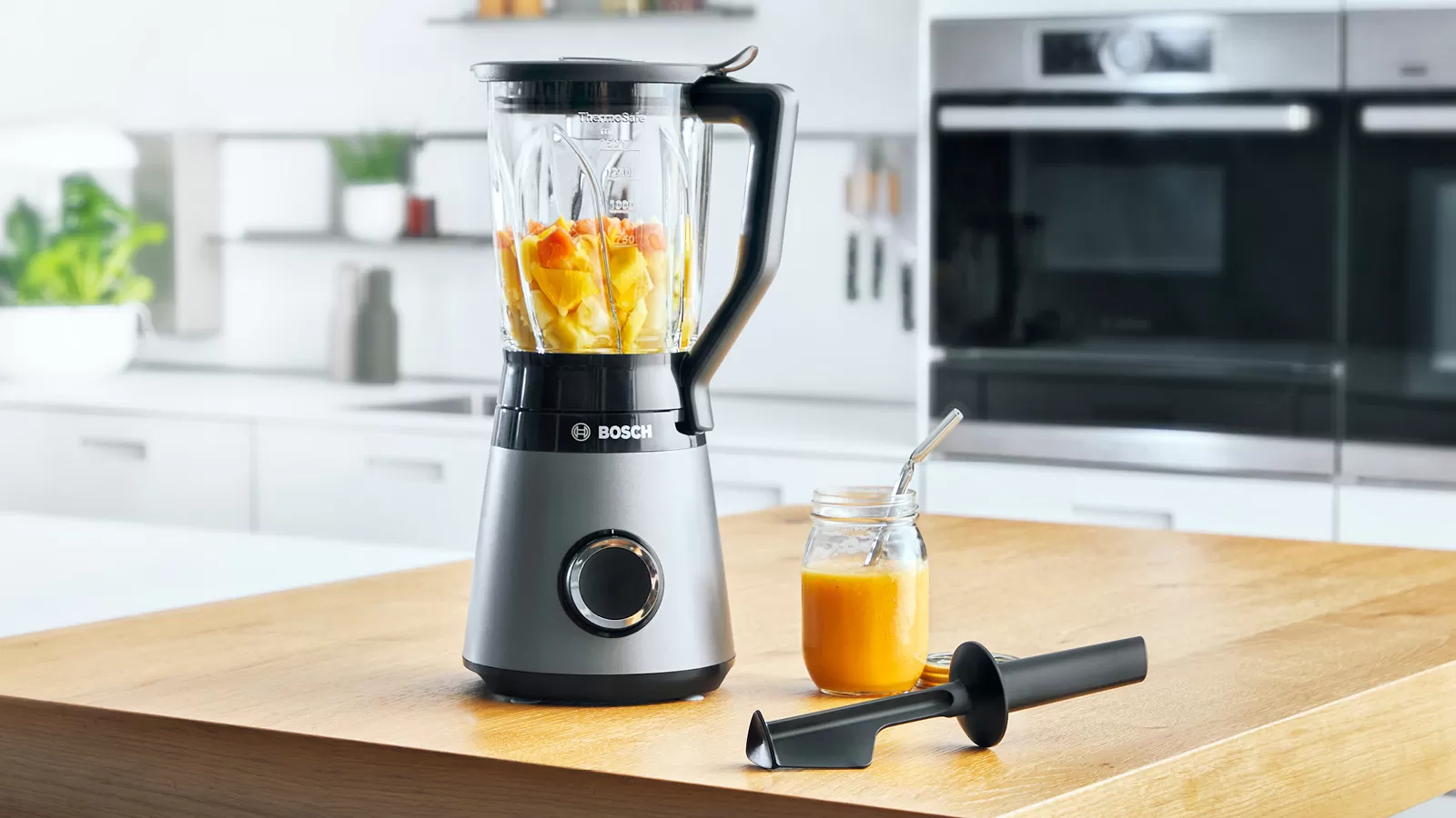 Ein Bosch-Mixer mit orangefarbenen und gelben Zutaten. Es gibt ein Glas.