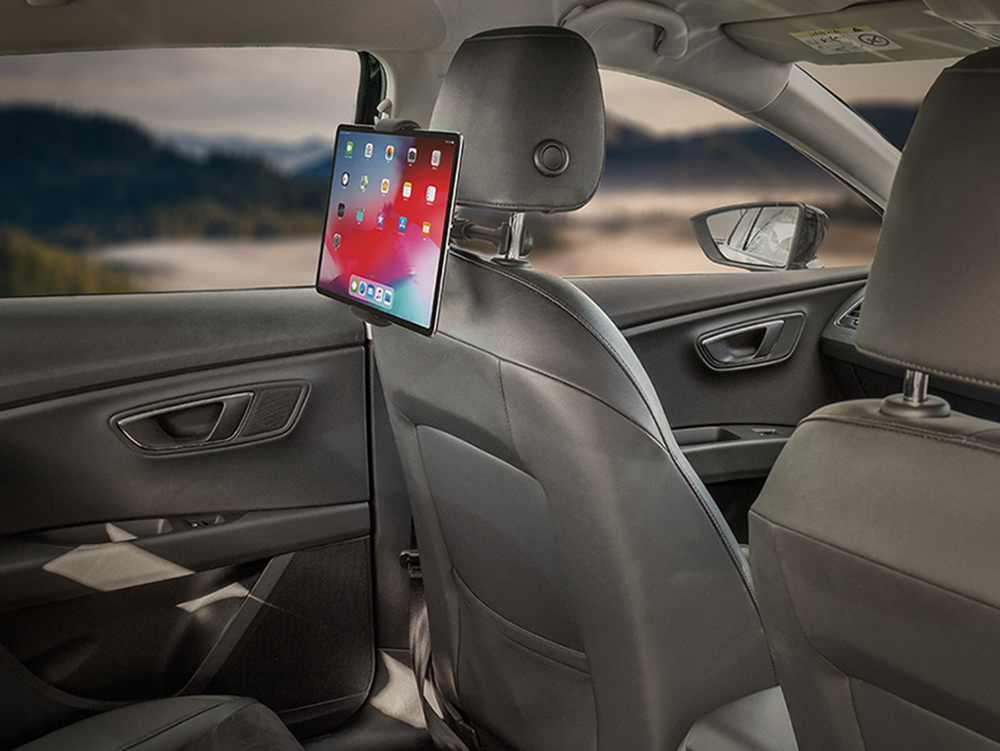 A tablet mounted to a car headrest. The tablet shows a screen. The car interior is visible.