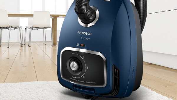 Blauer Bosch Serie 6 Staubsauger auf weißem Teppich. Im Hintergrund Tisch und Stühle.
