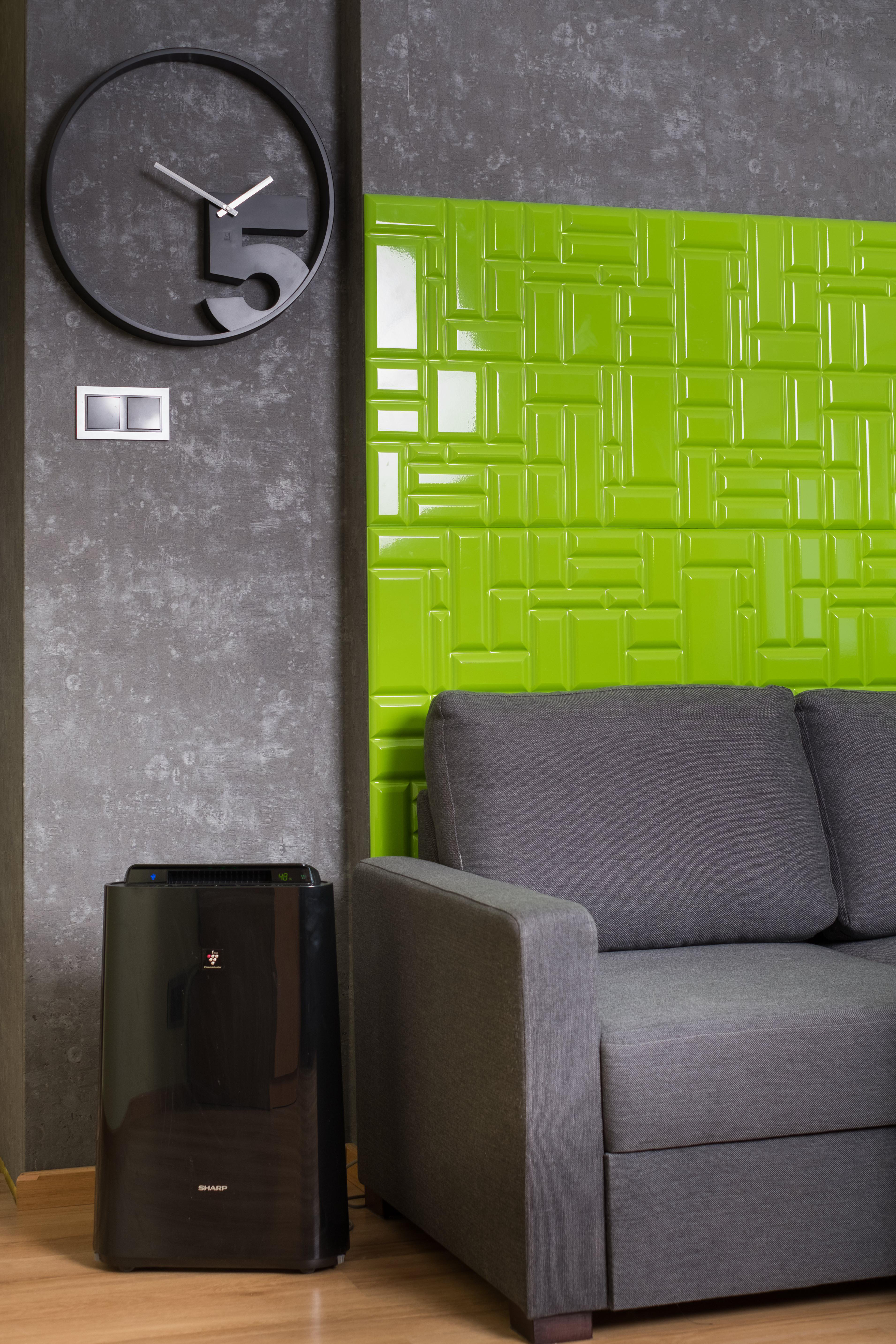 Ein Wohnzimmer mit grauem Sofa, grüner Wandverkleidung, einer Uhr und einem Luftreiniger auf dem Boden.