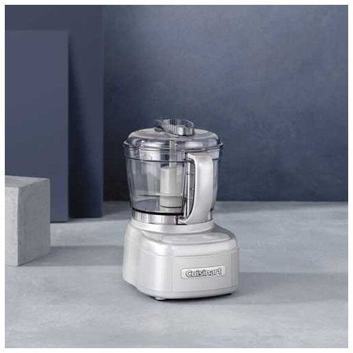 Un petit robot culinaire blanc sur une surface contre un fond bleu et gris.